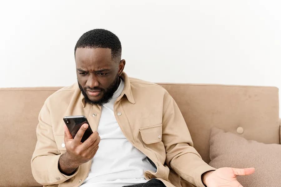 un homme allongé sur un canapé, un téléphone portable à la main