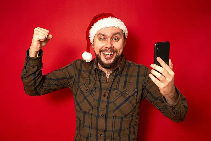 Un homme adulte portant un bonnet de Père Noël, tout excité, tenant un téléphone portable