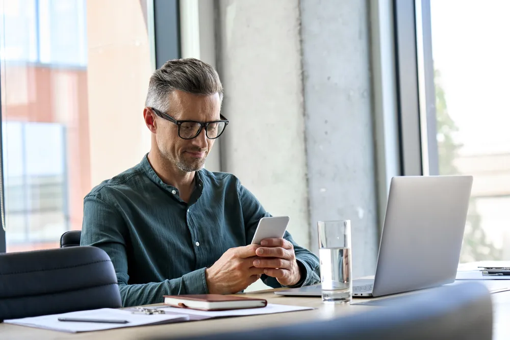 un homme regardant son smartphone tout en travaillant sur son ordinateur portable