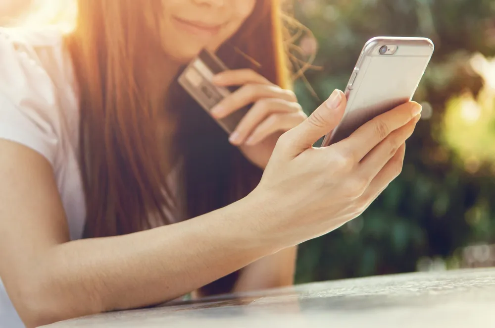 une jeune fille regardant son téléphone portable, une carte bancaire à la main