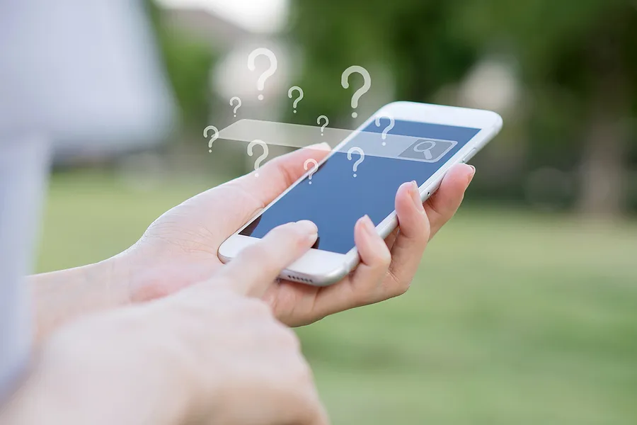 des mains tenant un smartphone dont la barre de recherche est vide et comportant de nombreux points d'interrogation