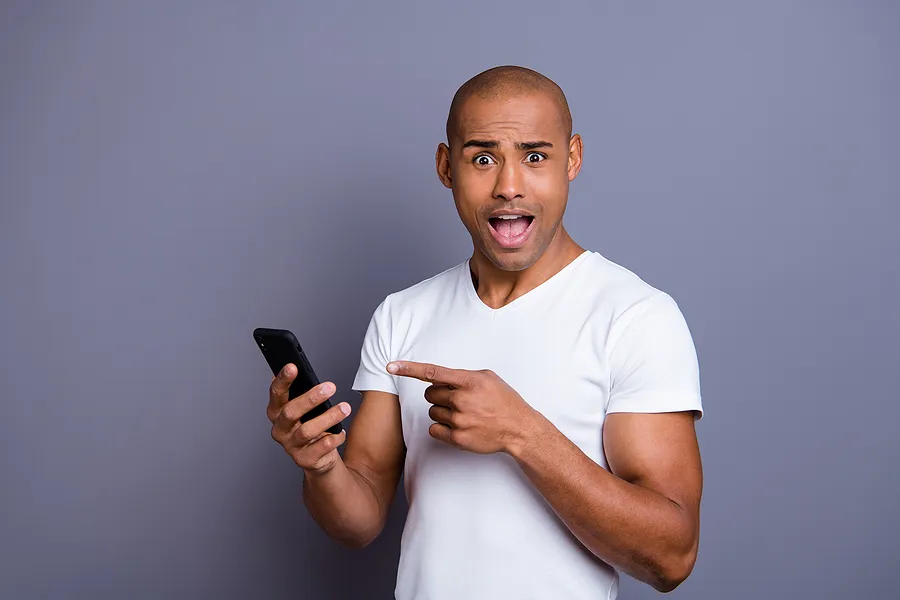 Un homme tenant un téléphone portable, l'air surpris