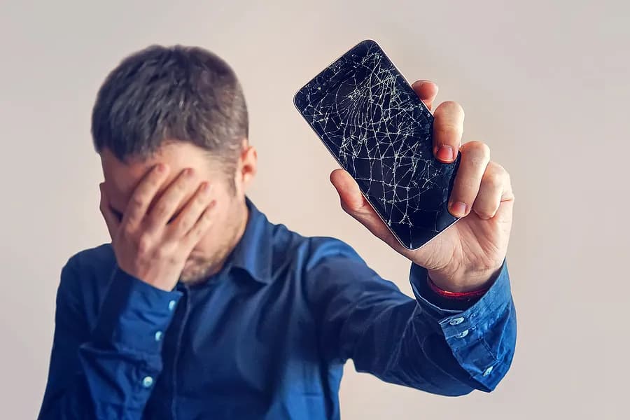 Un homme se couvrant les yeux et tenant son téléphone portable à distance de lui.