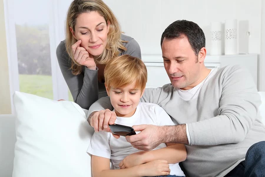 Une mère, un père et leur enfant regardent un téléphone portable.