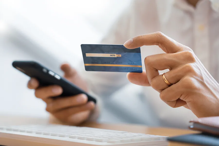 Des mains tenant un téléphone portable et une carte bancaire.