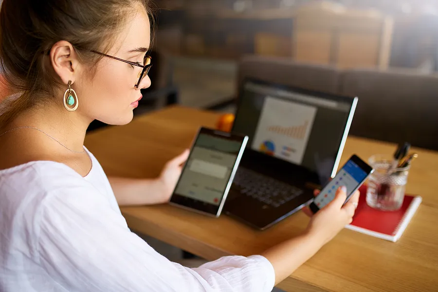Une femme avec un téléphone, une tablette et un ordinateur portable.