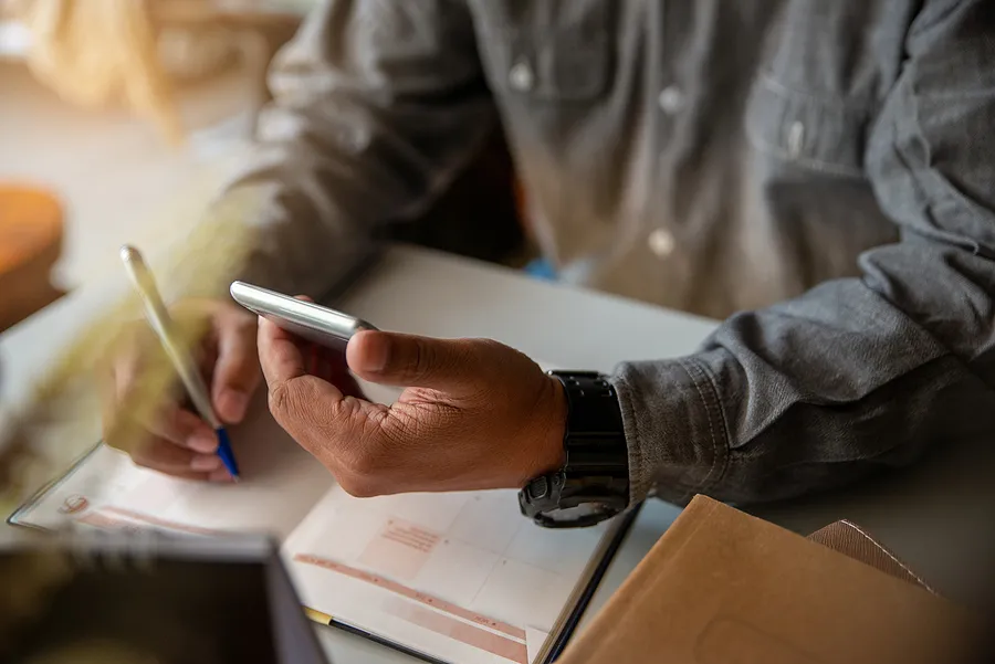 Personne tenant un téléphone portable tout en écrivant dans son agenda.
