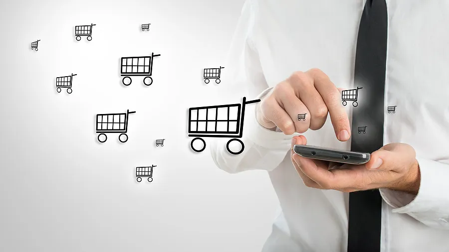 Un homme d'affaires utilisant un smartphone sur lequel figurent des icônes représentant des caddies, symbolisant le commerce électronique mobile et les achats de téléphones en ligne.