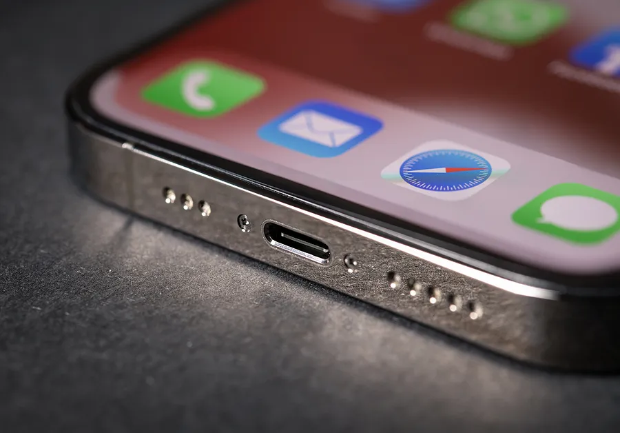 Gros plan sur le port de recharge d'un iPhone, avec des icônes d'applications visibles à l'écran, illustrant les problèmes de recharge de l'iPhone.