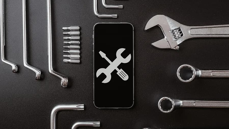 Outils de diagnostic et concept de réparation de smartphone, avec l'écran du téléphone affichant une icône représentant une clé et un tournevis, entourée d'outils métalliques.
