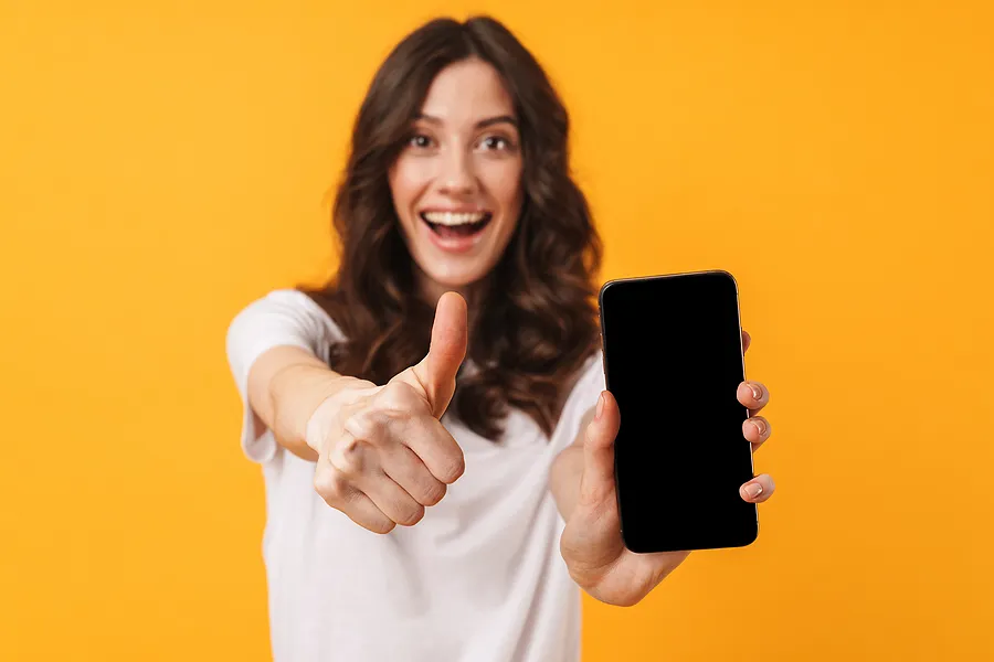 Une femme souriante tenant un smartphone et levant le pouce, symbolisant la réussite du processus de vérification et de certification par téléphone.