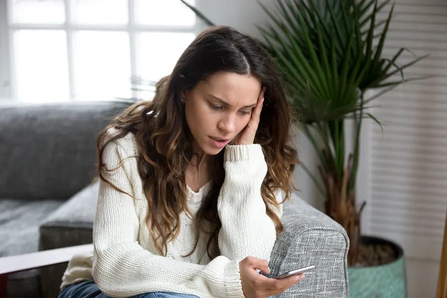Une femme inquiète regardant son smartphone, illustrant l'importance de consulter les rapports sur les téléphones d'occasion et de bien comprendre l'historique d'un appareil avant de l'acheter.