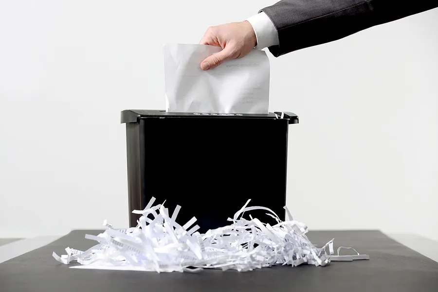 Une personne insérant manuellement des documents dans un broyeur à papier, illustrant ainsi la destruction certifiée des données et l'élimination sécurisée des informations sensibles.